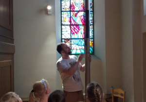 dzieci stoją przy organach na chórze w kościele, pan od rytmiki pokazuje dzieciom piszczałkę